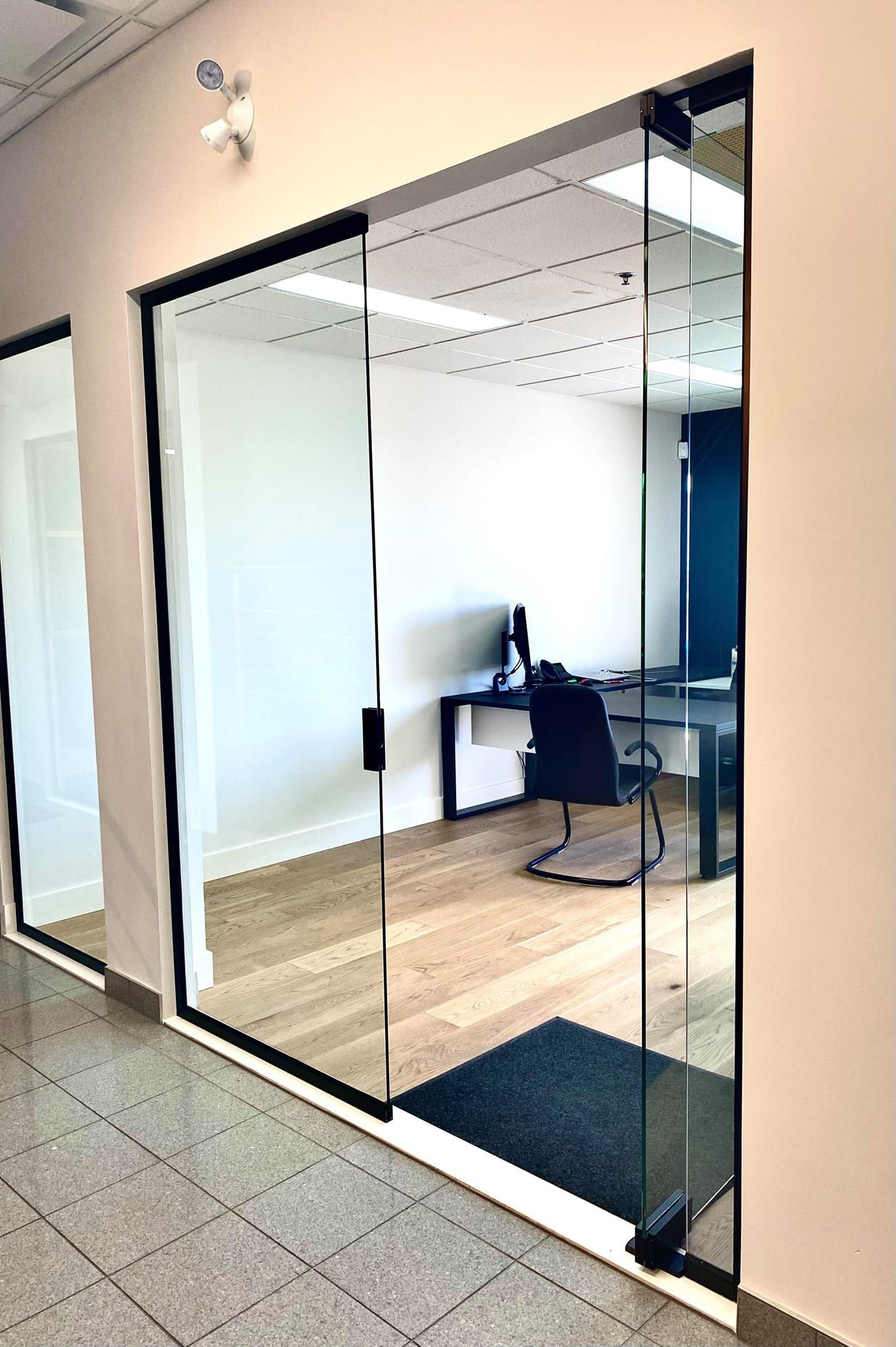 Un couloir avec portes coulissantes en verre menant à une pièce avec un bureau et une chaise.