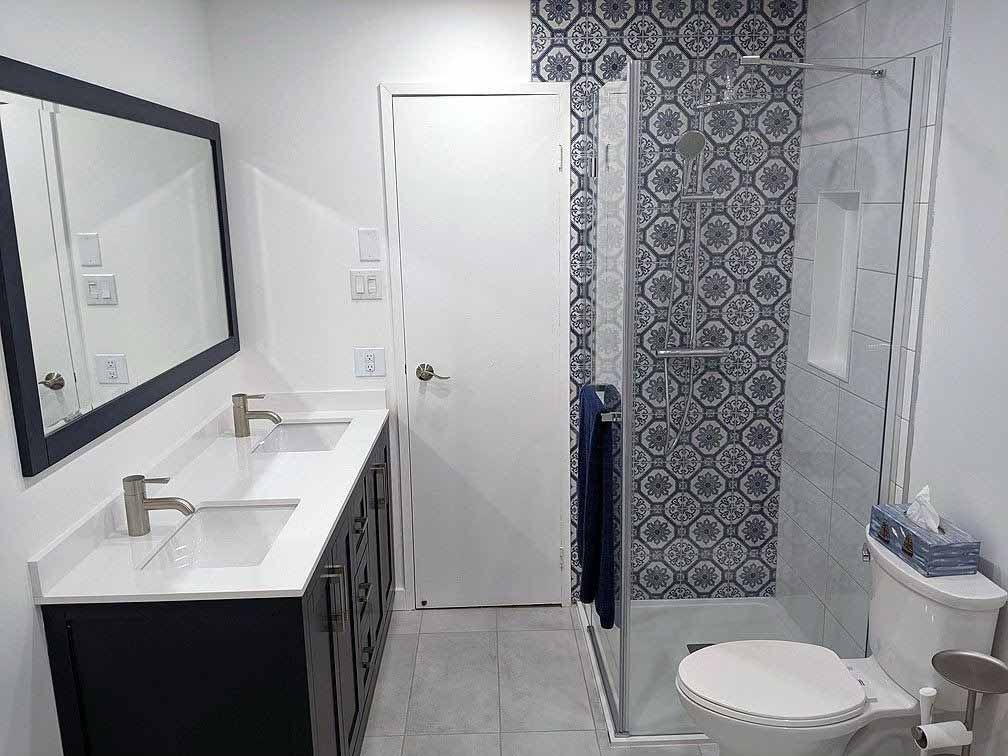 Salle de bain avec vanité foncée, carrelage de douche à motifs et toilettes.