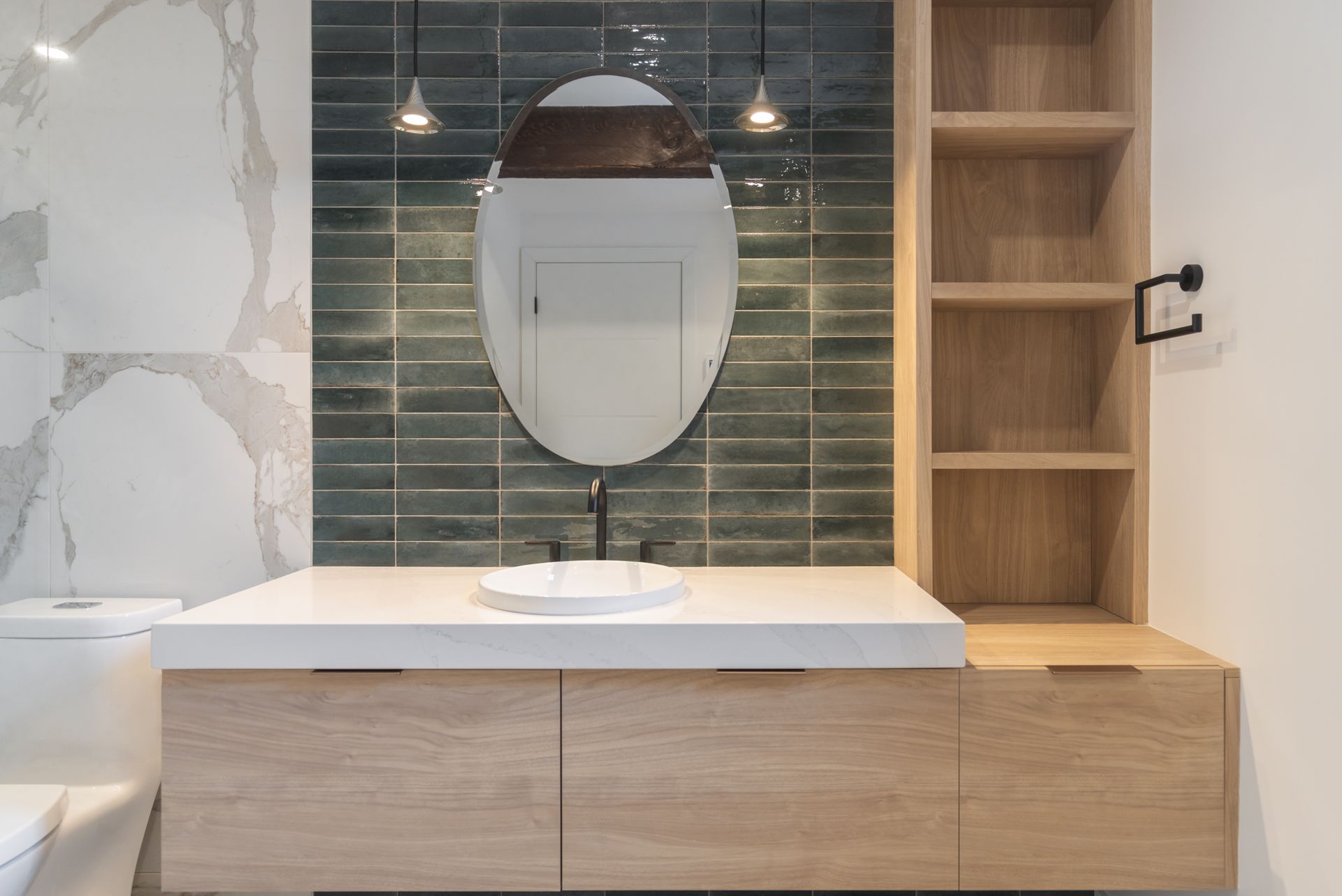 Salle de bain avec miroir ovale, vanité en bois, comptoir blanc et dosseret carrelé bleu sarcelle.