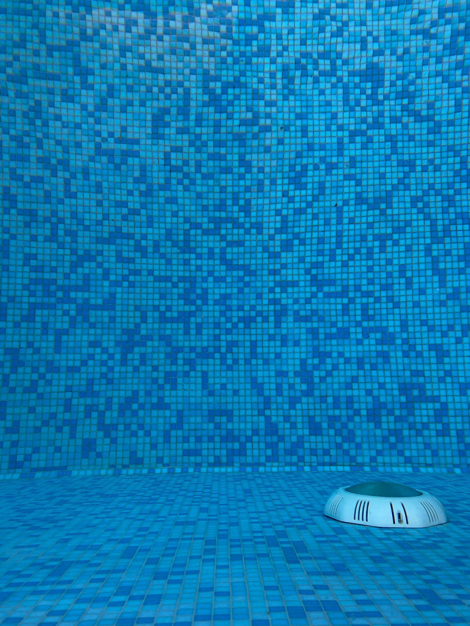 Interior de una piscina revestida de azulejos azules, con una pequeña fuente redonda o un desagüe en el suelo