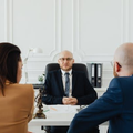 Three people in a formal office meeting, with one person seated across from two others.