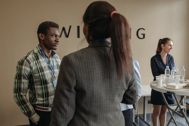 People networking in a bright office, with a drinks table and a wall sign in the background.