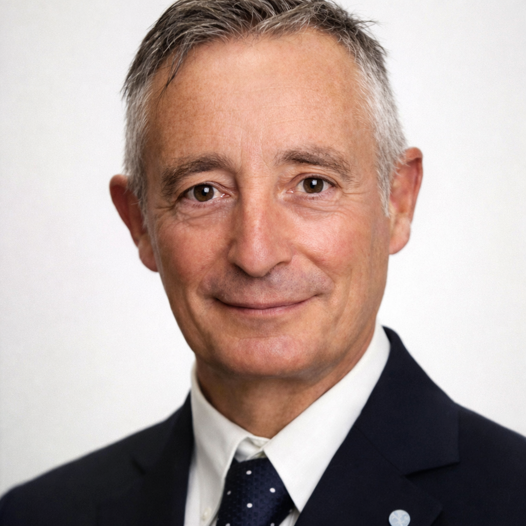 Man in a dark suit with a white shirt and patterned tie smiling at the camera.