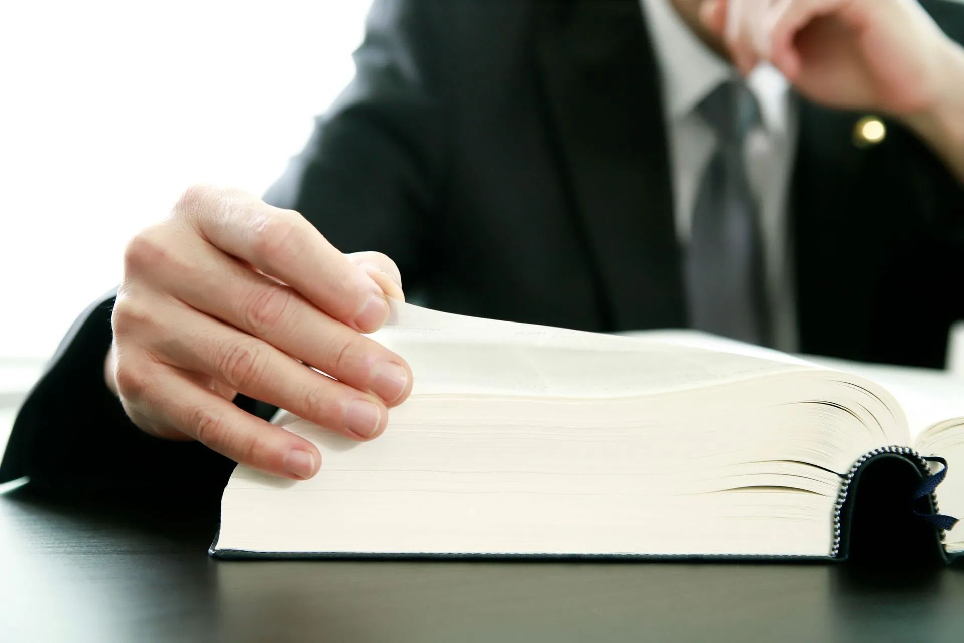 Person in suit flipping through large book at desk.