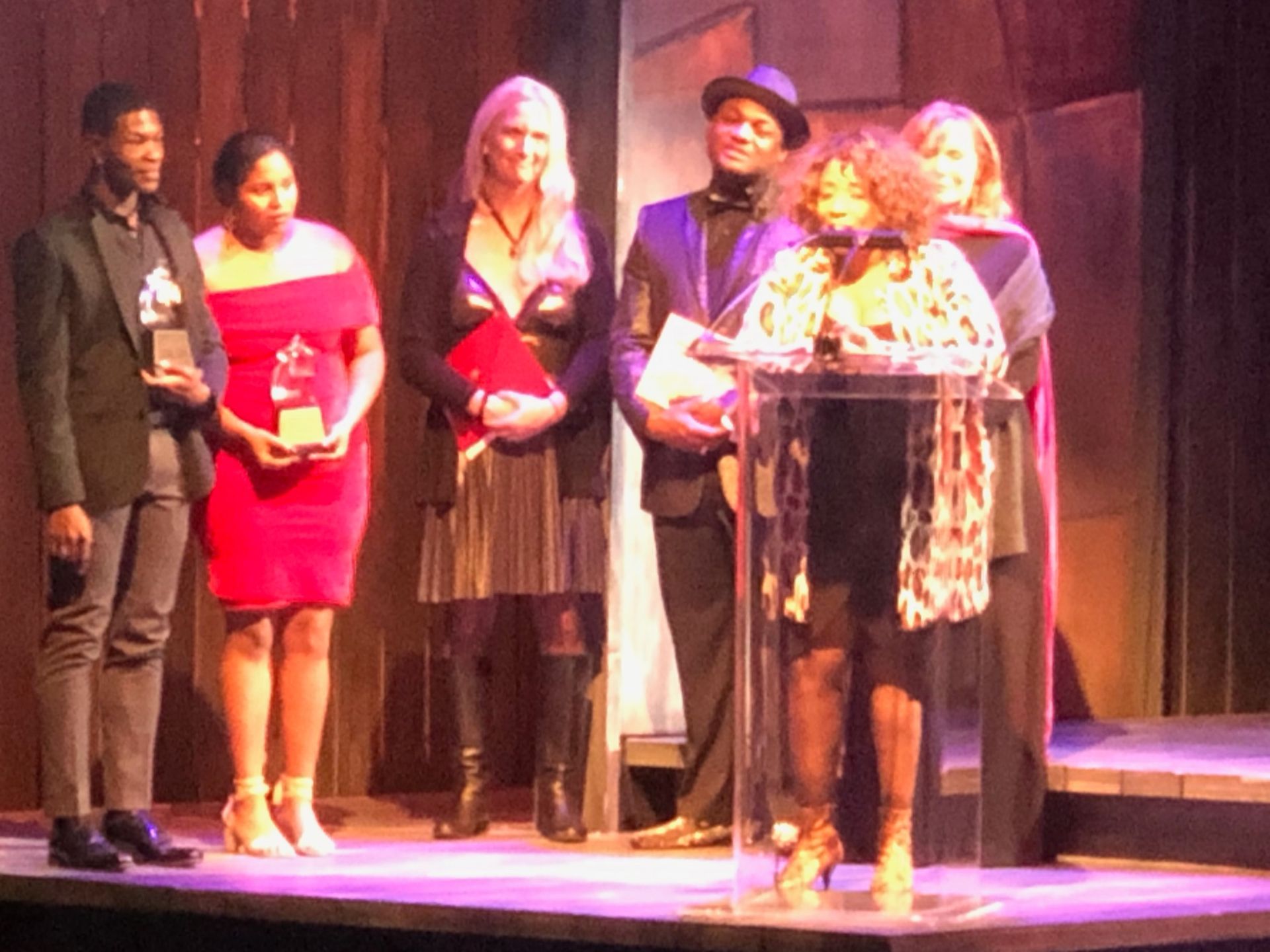 Group of people on stage, accepting awards. Woman at podium speaking.
