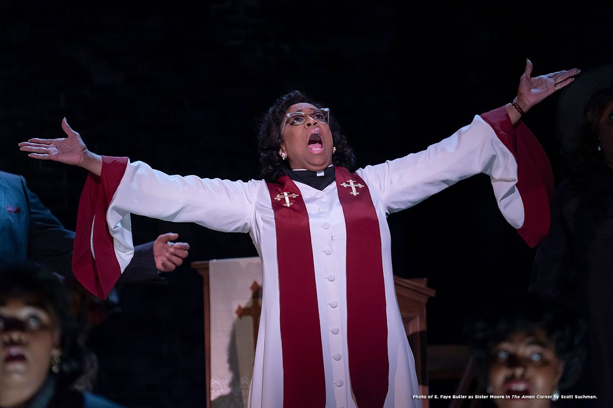 Woman in white robe with red sash, arms raised, singing in a church.