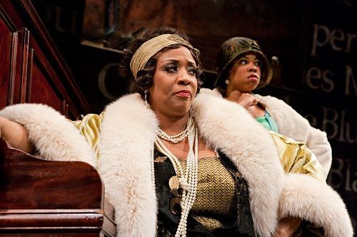 Two Black women in vintage attire, one with a fur, gazing intently.