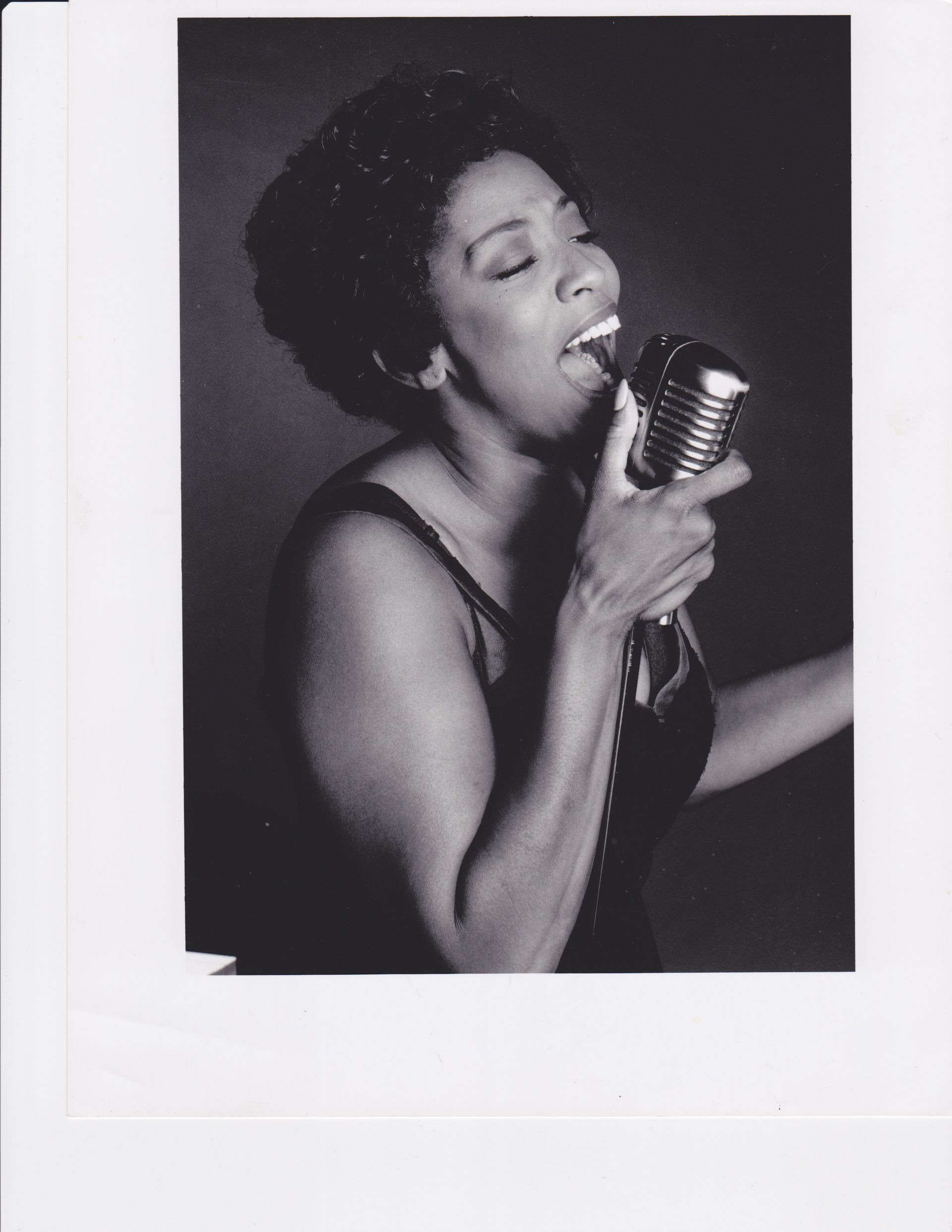Woman singing into a vintage microphone, mouth open. Black and white photo.