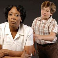 Woman in white top and young boy in plaid shirt, both looking toward the camera with serious expressions.