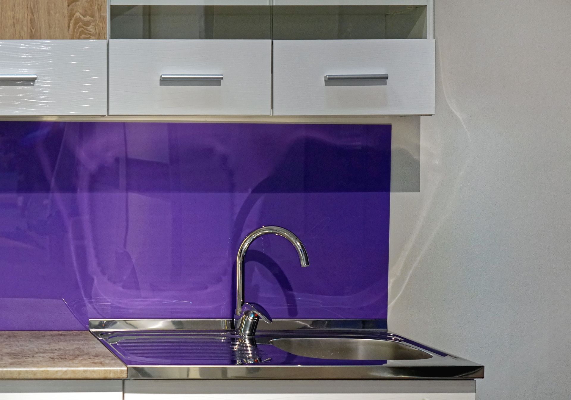 Purple glass splashback behind a kitchen sink. 