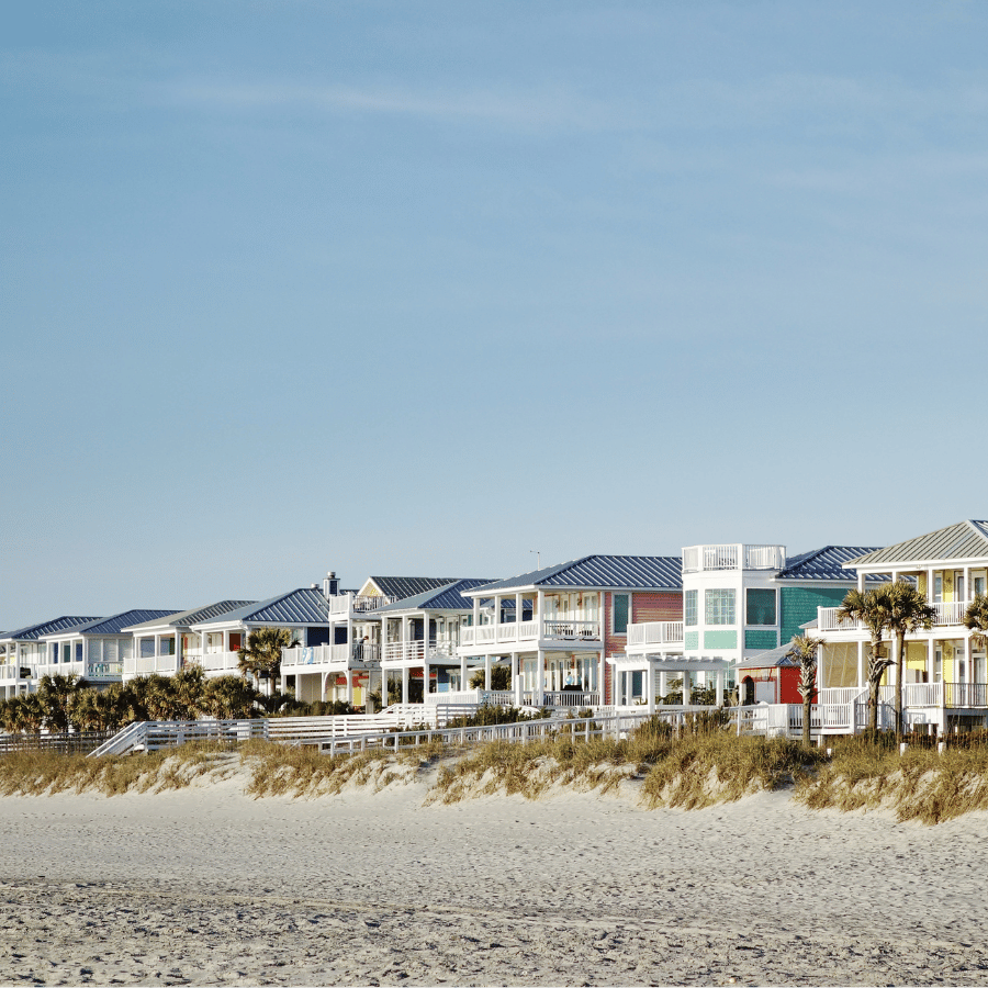 Beachfront row houses with blue roofs behind sand dunes under a clear sky