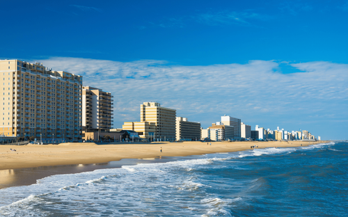 Sunny beach with waves, sandy shore, and tall beachfront buildings under a blue sky