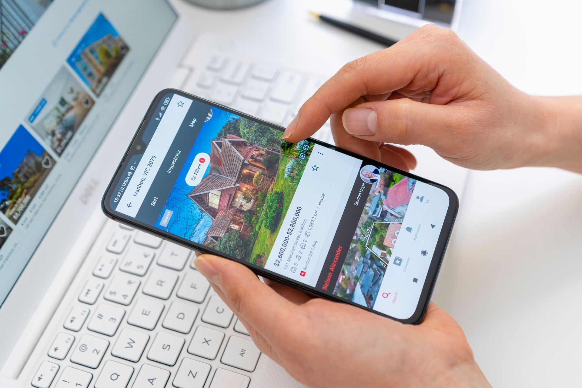 Hands using a smartphone over a keyboard, browsing a colorful website on a desk.
