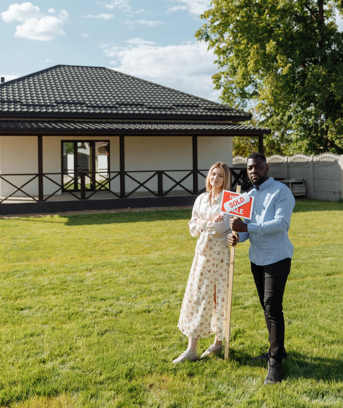 Two people standing on a lawn in front of a house, holding a red-and-white drone controller.