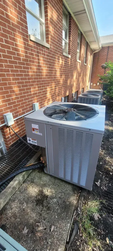 Multiple air conditioning units sit on a concrete slab next to a brick building.