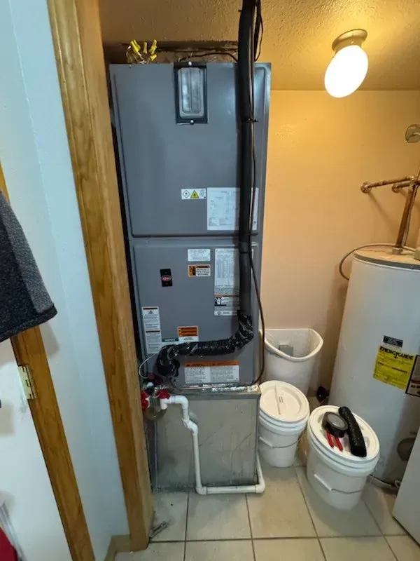 Furnace and water heater in a utility closet. Grey furnace, white water heater, tools, and a filter on the floor.