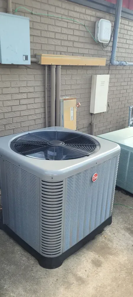 An air conditioning unit against a brick wall with other utility boxes and pipes.