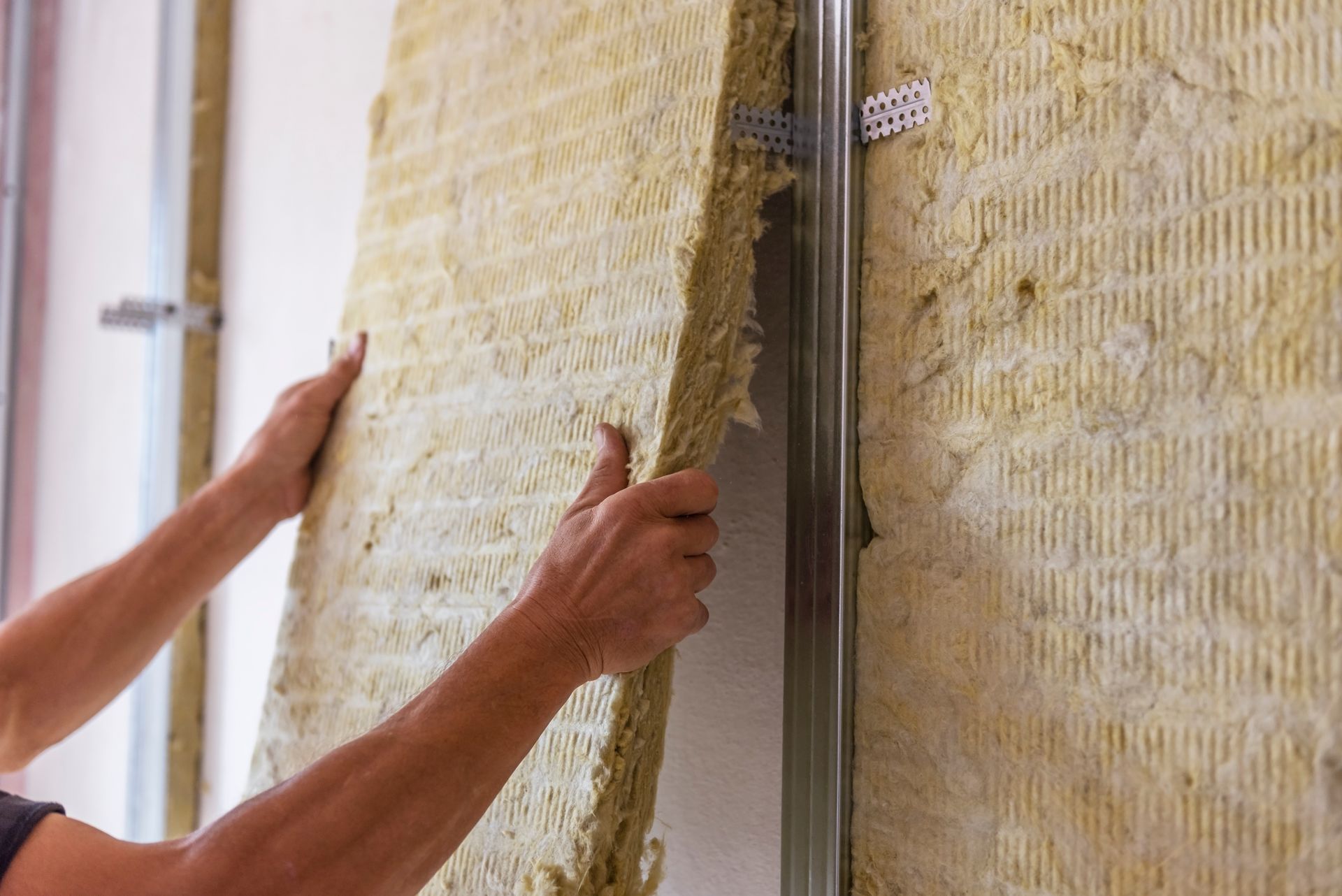Hands installing insulation between metal studs on a wall.