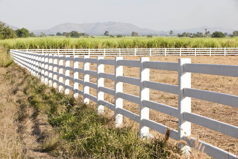 A White Fence Surrounds a Field of Grass and Dirt — Hazells Farm & Fertilizer Services in Taminda, NSW