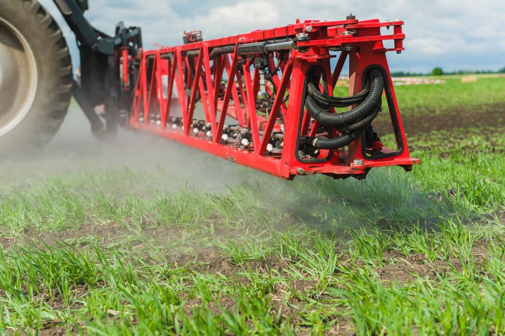 A Tractor Is Spraying a Field with A Sprayer — Hazells Farm & Fertilizer Services in Taminda, NSW