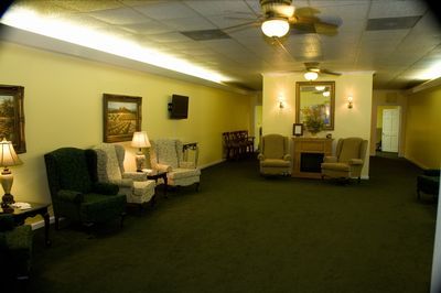 a living room with green chairs , a fireplace and a ceiling fan .