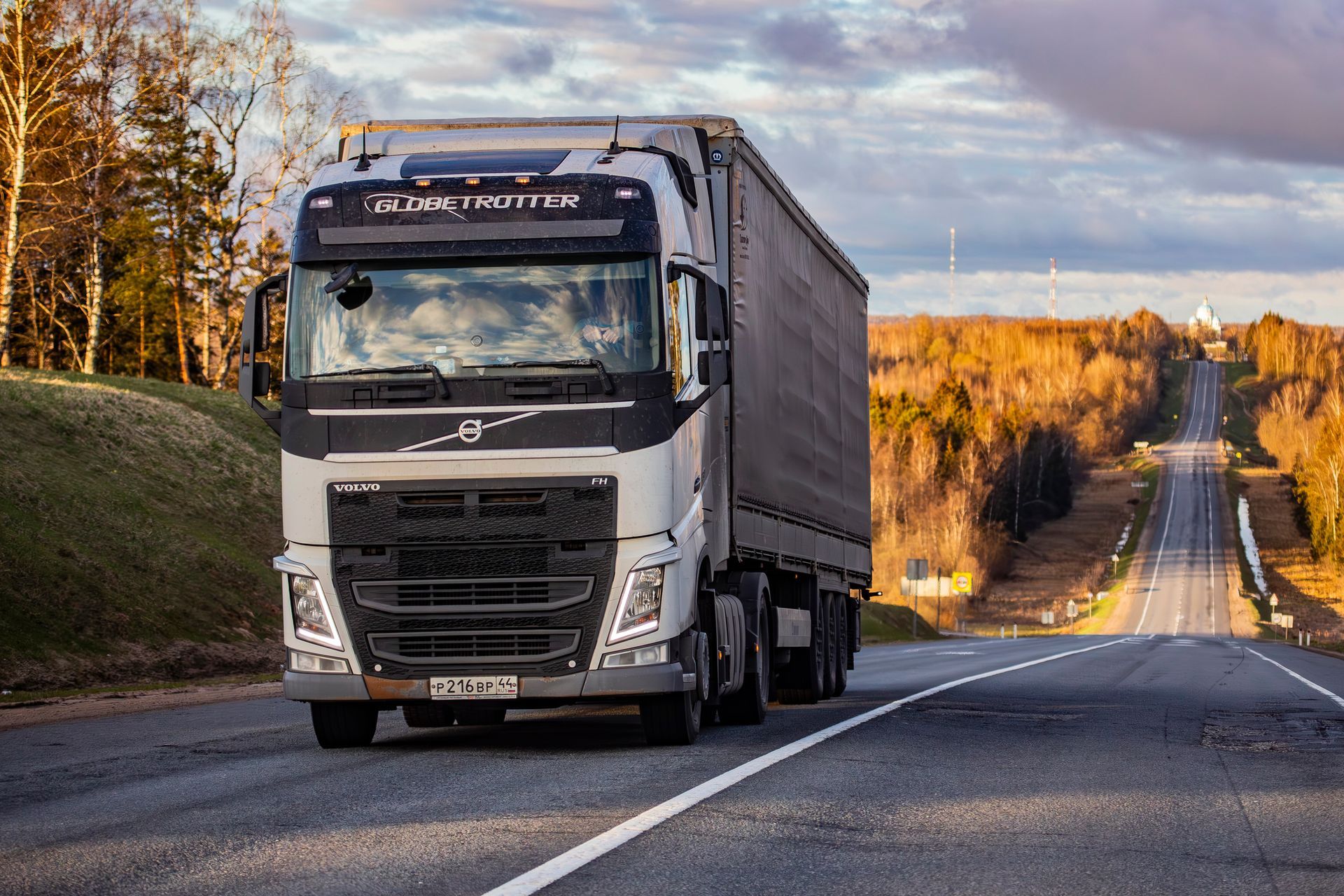 White semi-truck driving on a rural road with autumn trees and hills in the background
