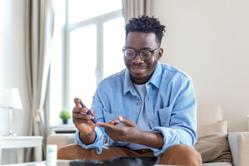A person in a blue shirt sits on a couch, smiling while using a blood glucose meter to test their blood sugar level.