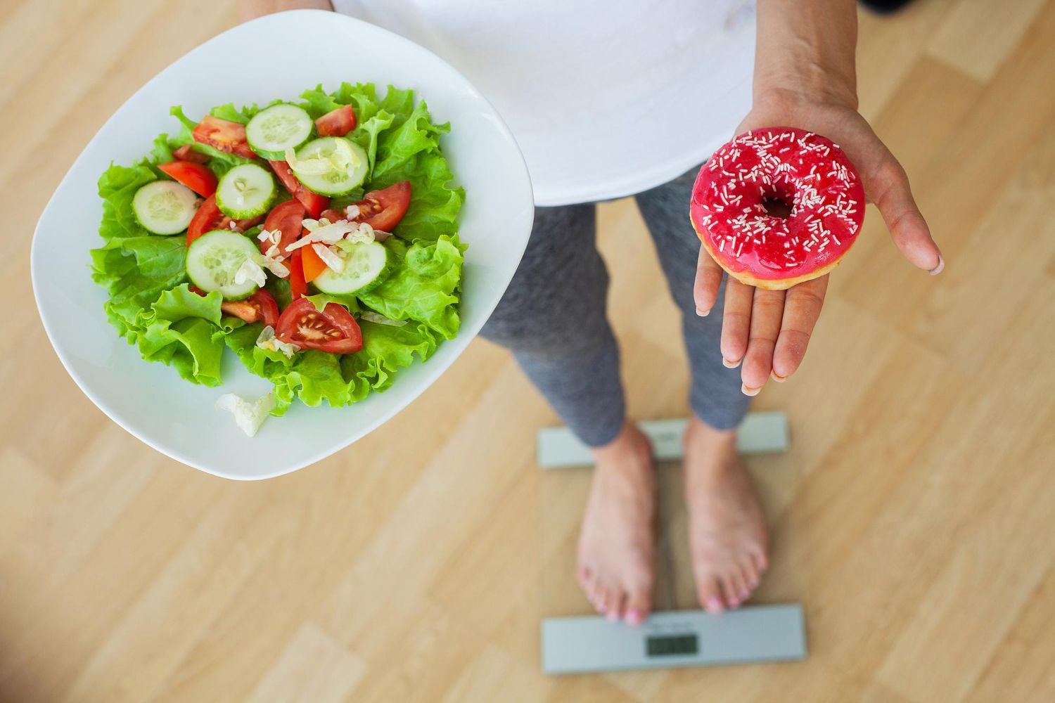 Person on a scale holding a salad bowl and a cupcake, suggesting healthy eating and indulgence