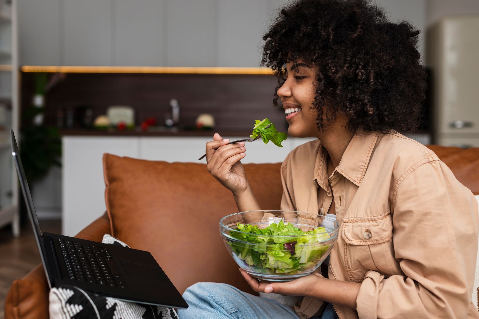 a woman is eating a salad while looking at a laptop