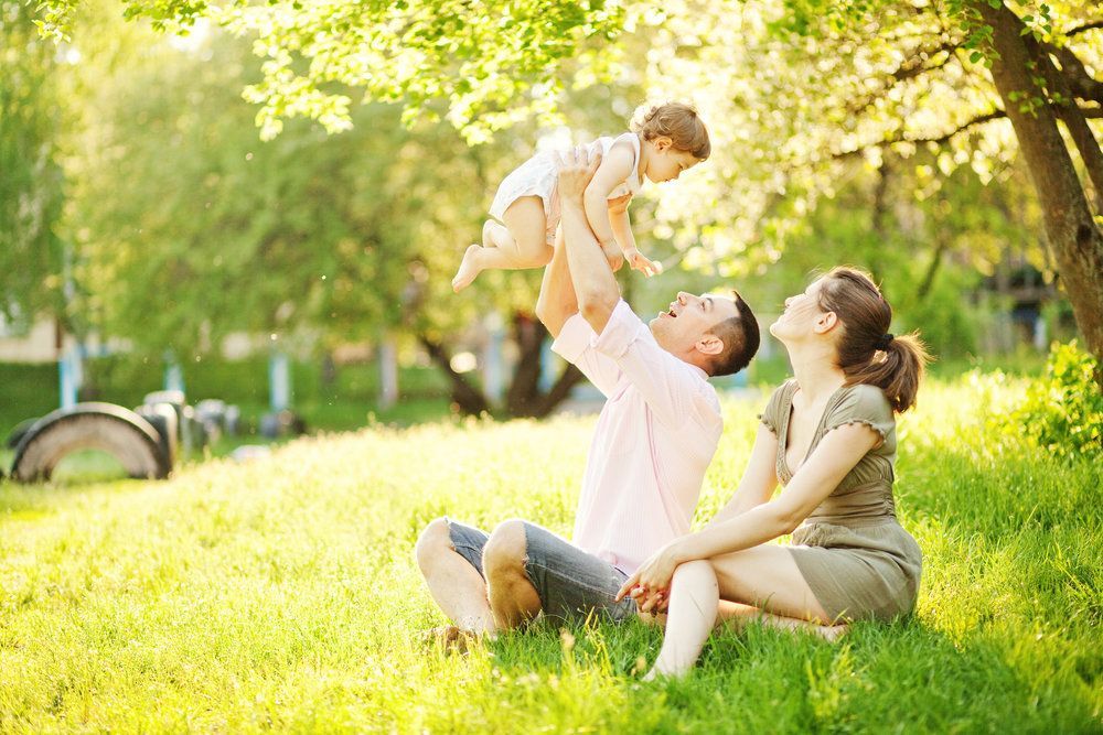 a man and woman are sitting in the grass holding a baby in the air