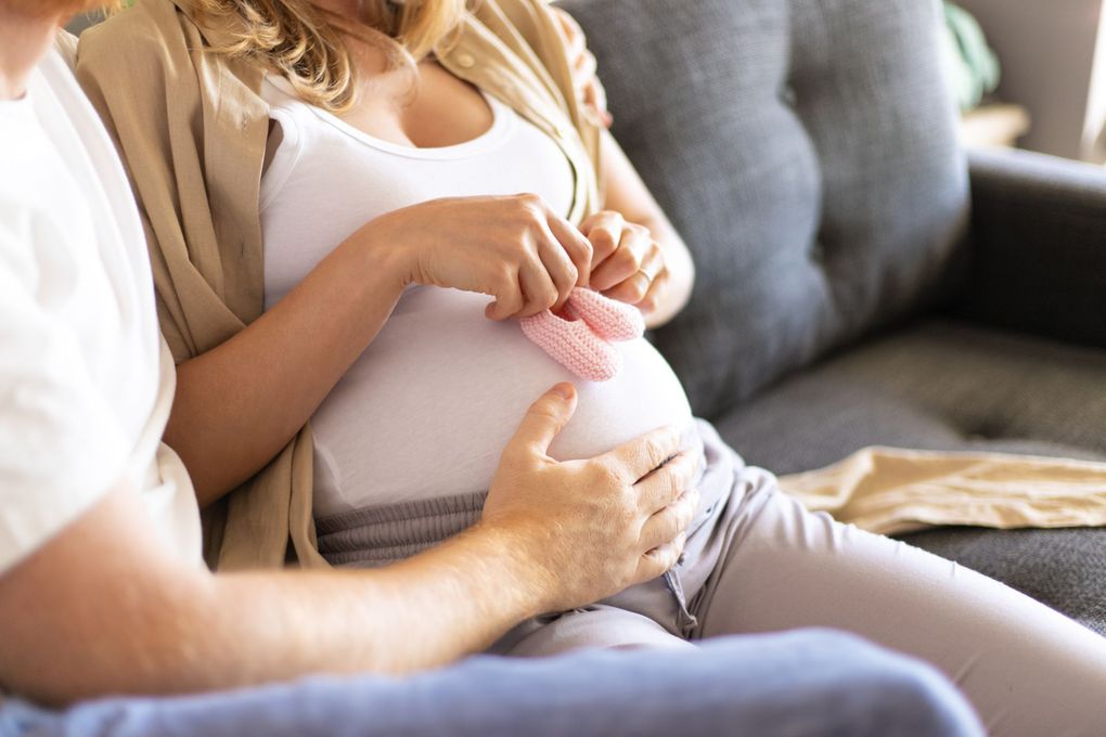 a pregnant woman holds a pair of pink baby shoes on her belly