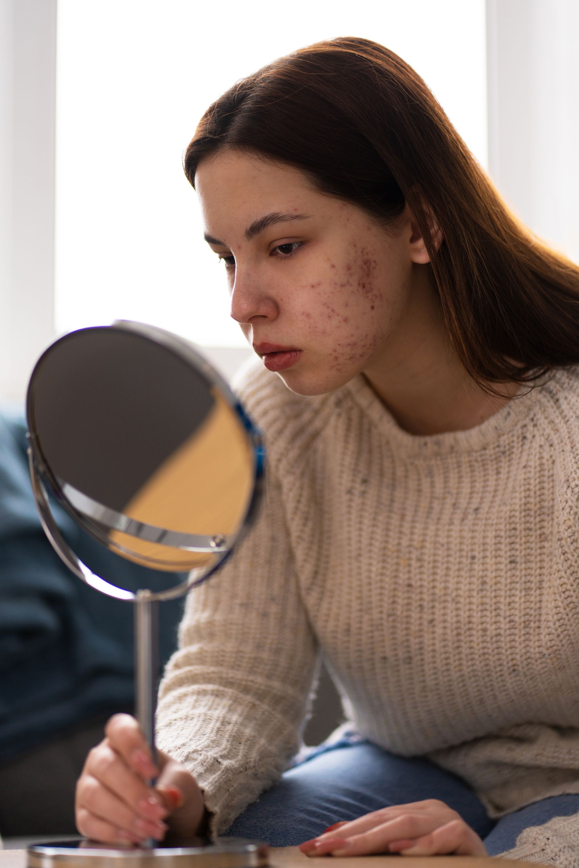 Person applying makeup while looking into a round mirror in a bright room