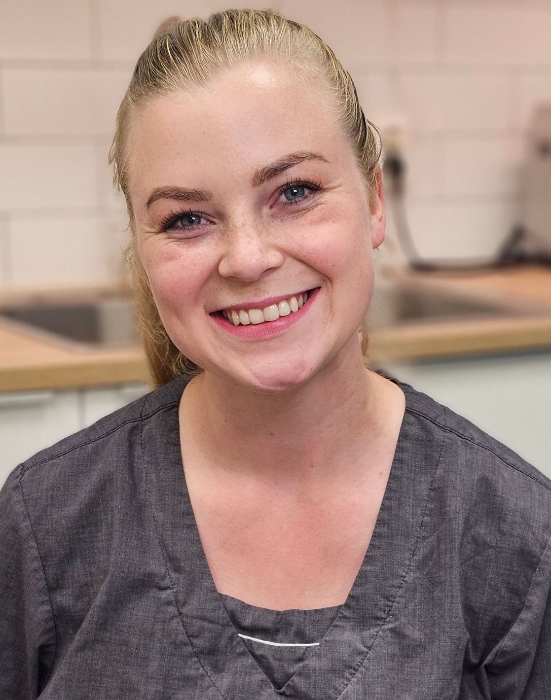 En kvinne med langt blondt hår smiler i en stue.