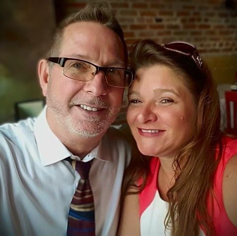 A man and a woman are posing for a picture together . the man is wearing glasses and a tie.