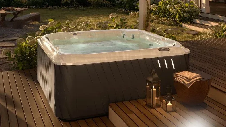 Backyard hot tub on a wooden deck, lit warmly at dusk, with lanterns and a towel nearby