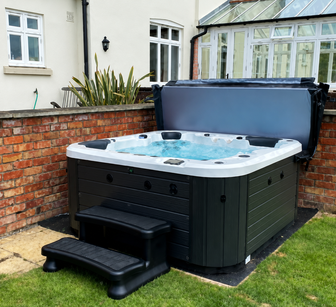 Black outdoor hot tub with steps in a small brick-walled garden beside a house