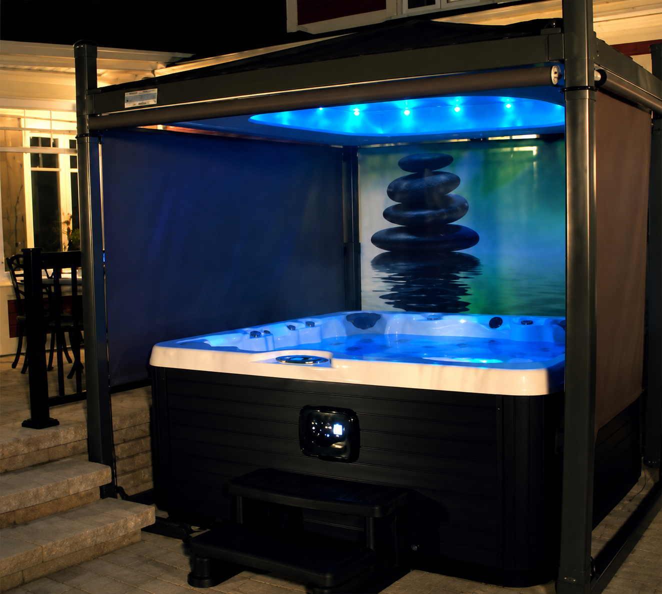 Blue-lit outdoor hot tub with a stacked stone water feature, set in a covered patio area.