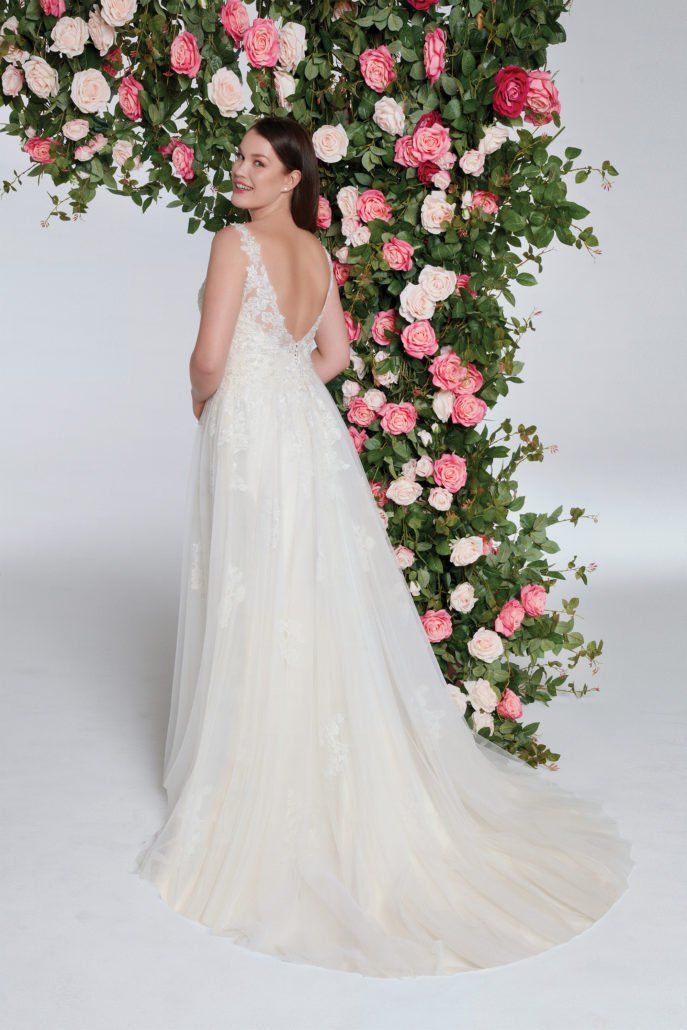 Eine Frau in einem Brautkleid steht vor einer Wand aus Blumen.