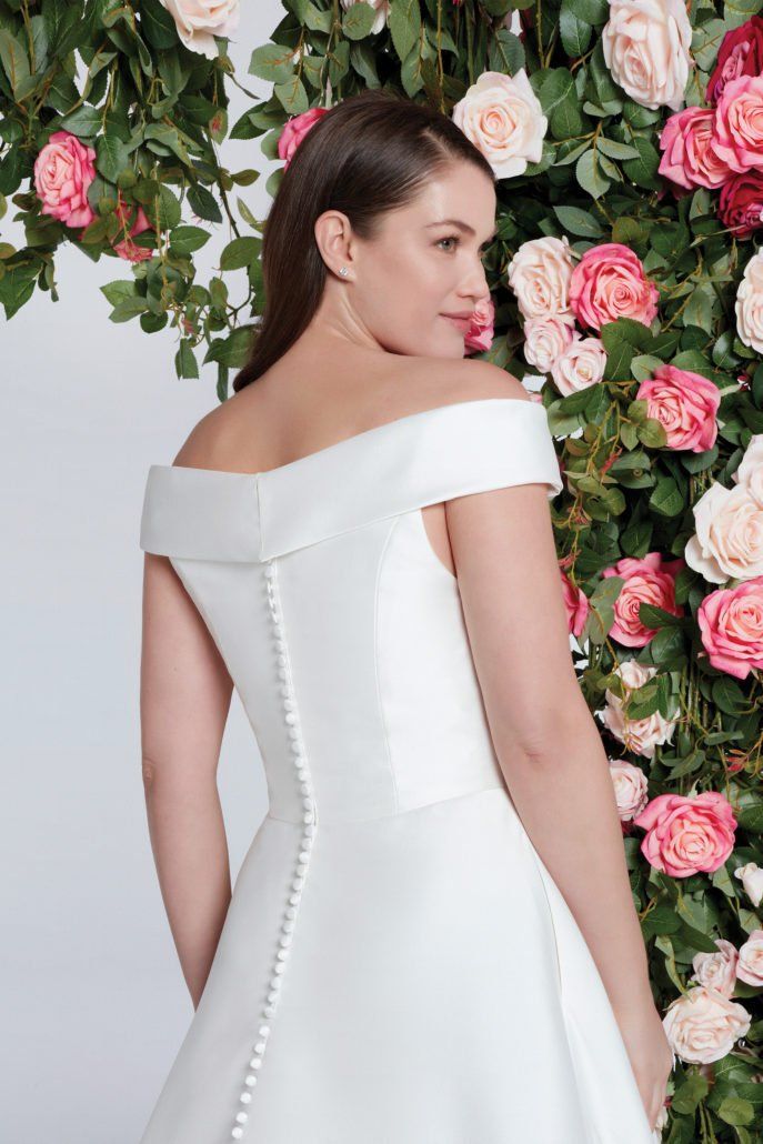 Eine Frau in einem weißen Brautkleid steht vor einer Wand aus Blumen.
