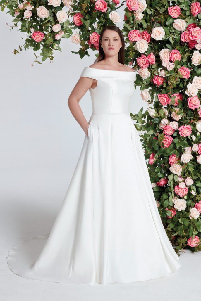 Eine Frau in einem weißen Kleid steht vor einer Blumenwand.