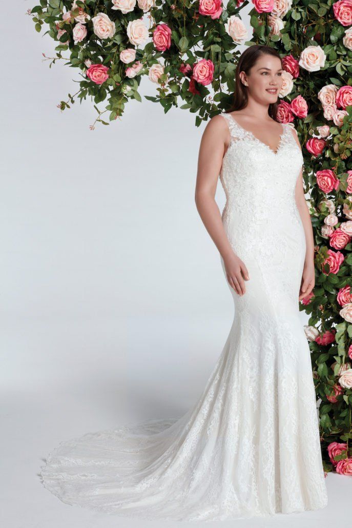 Eine Frau in einem weißen Hochzeitskleid steht vor einer Wand aus rosa Rosen.