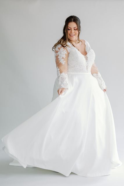 Eine Übergrößenbraut trägt ein weißes Hochzeitskleid mit langen Ärmeln.