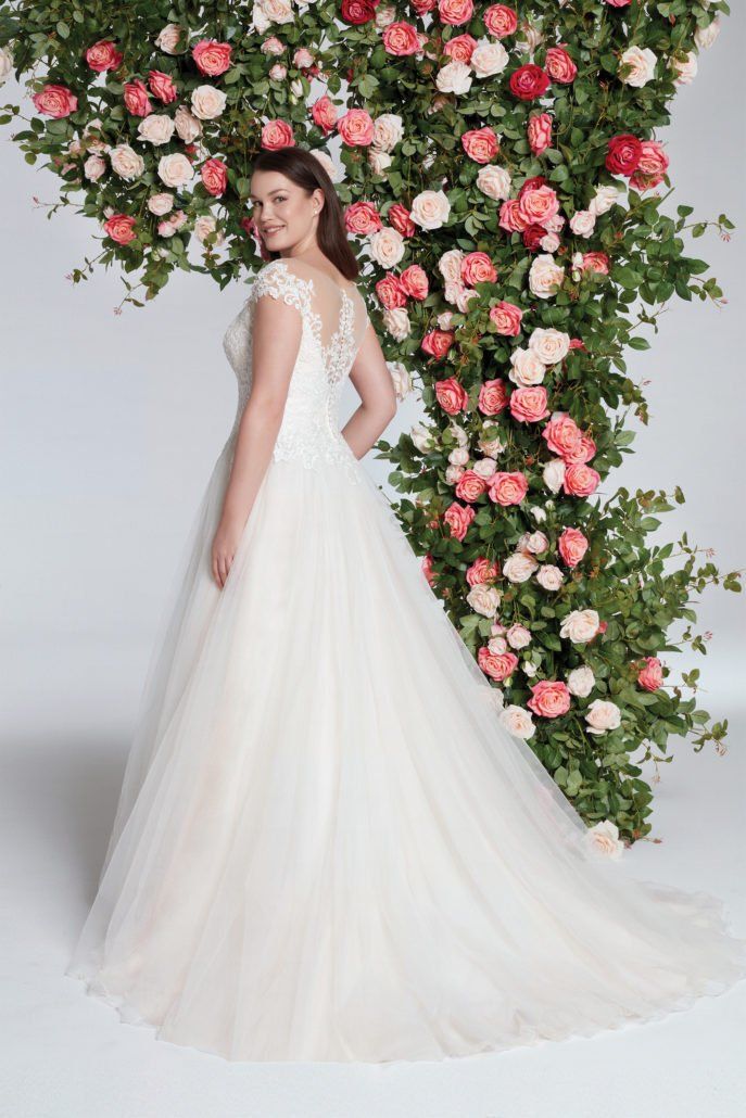 Eine Frau in einem Brautkleid steht vor einer Wand aus Blumen.