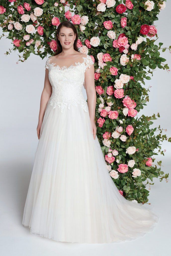 Eine Frau in einem weißen Brautkleid steht vor einer Wand aus Blumen.