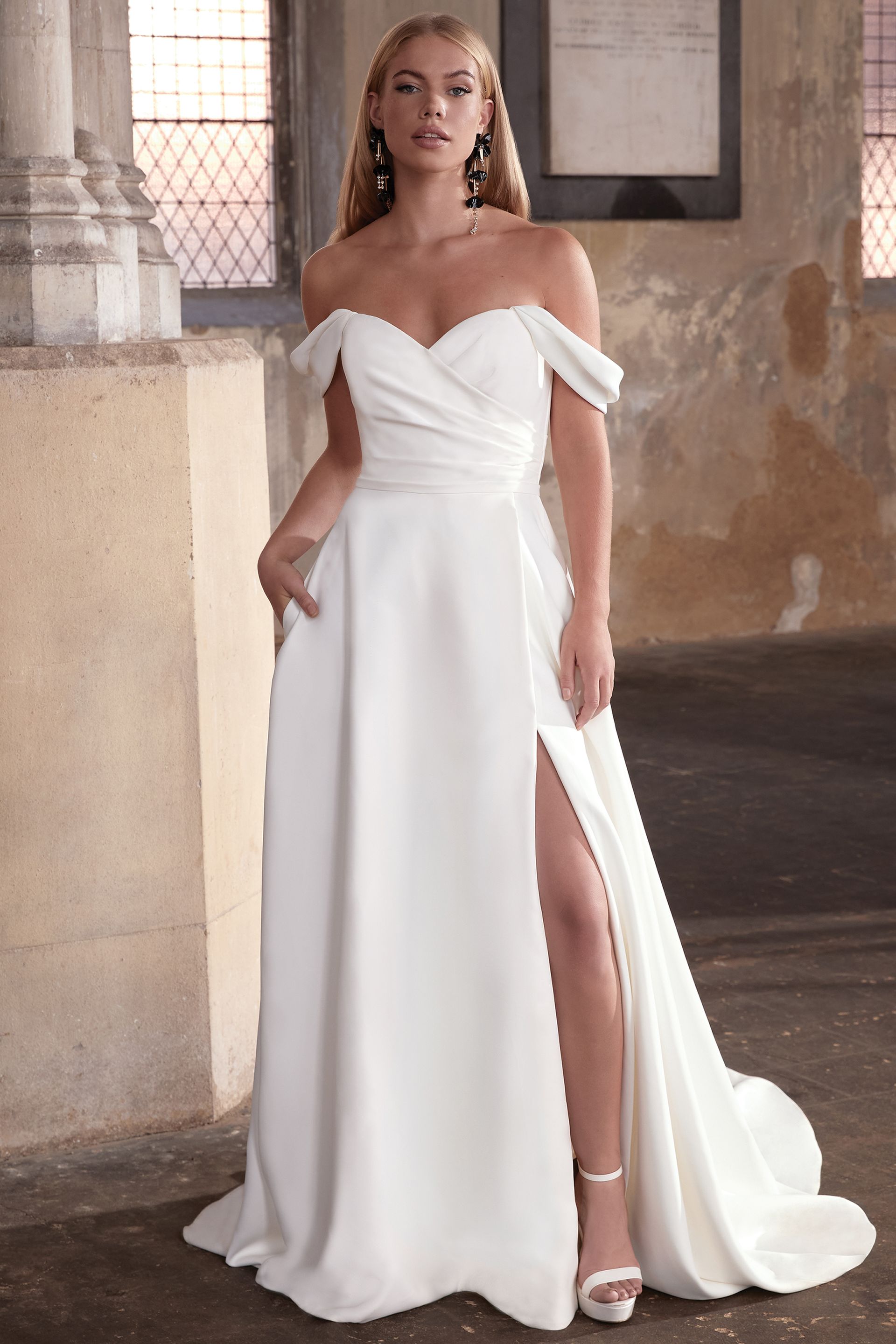 Eine Frau trägt ein weißes schulterfreies Brautkleid mit hohem Schlitz.