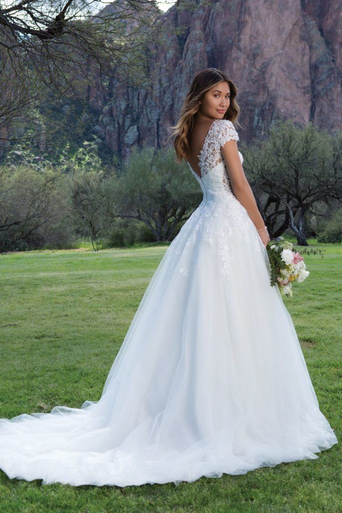 Eine Frau in einem weißen Hochzeitskleid steht auf einem Feld und hält einen Blumenstrauß in der Hand.