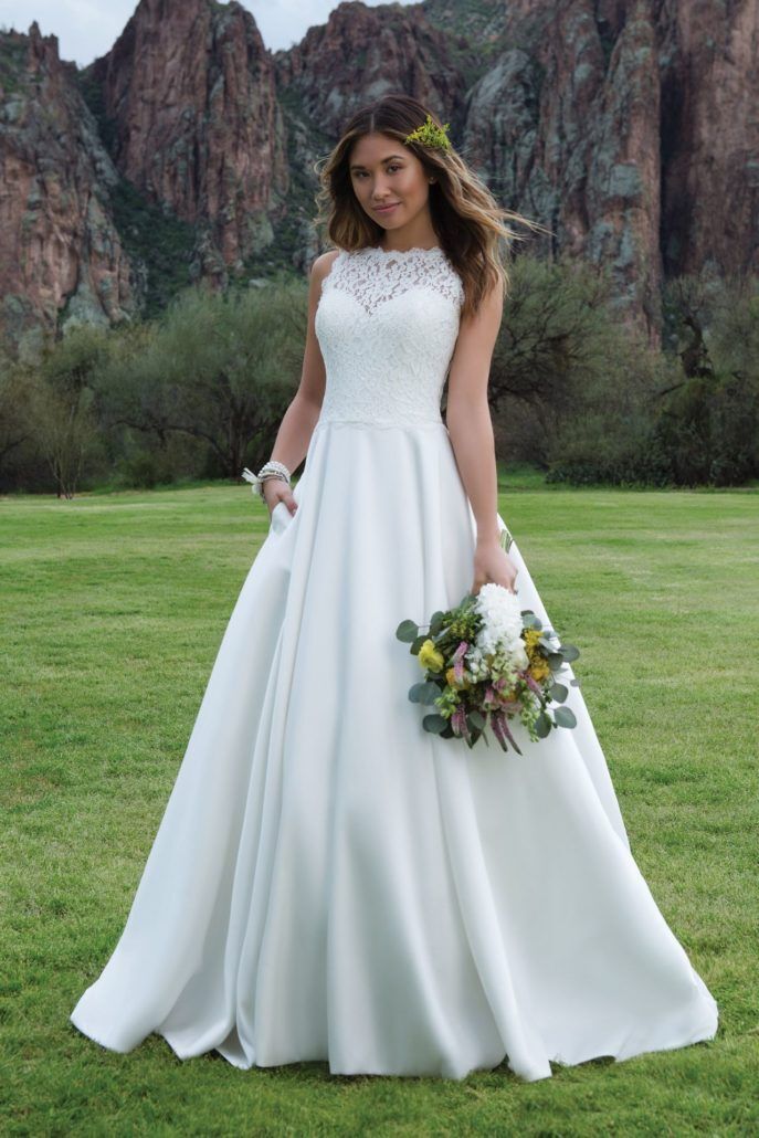 Eine Frau in einem weißen Hochzeitskleid steht auf einem Feld und hält einen Blumenstrauß in der Hand.