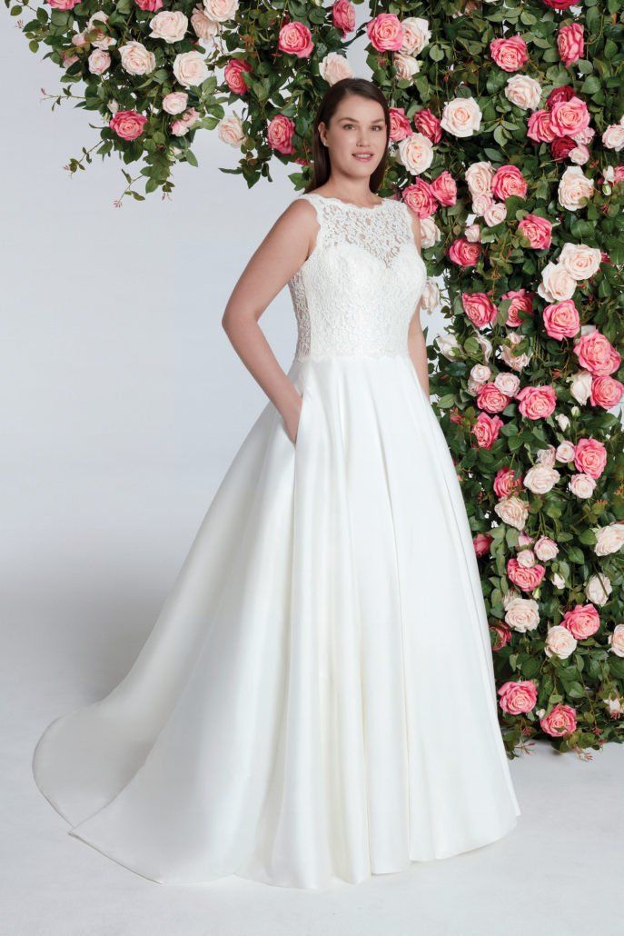 Eine Frau in einem weißen Hochzeitskleid steht vor einer Wand aus rosa Rosen.