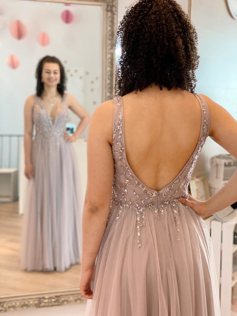 Eine Frau steht und trägt ein Kleid vor einem Spiegel.