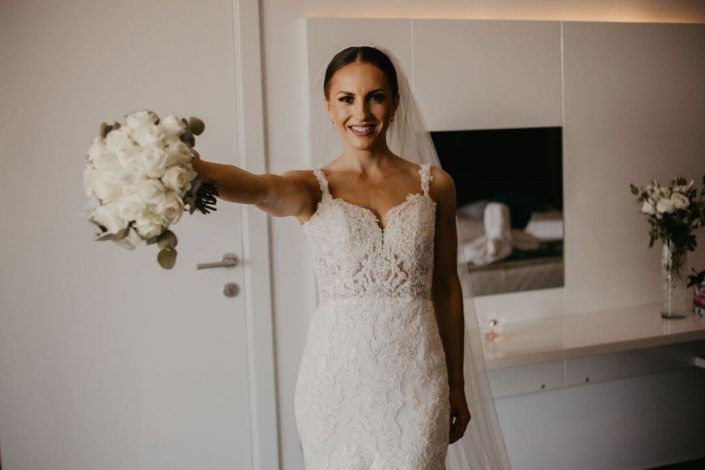 Eine Braut im Hochzeitskleid hält einen Strauß weißer Blumen in der Hand.